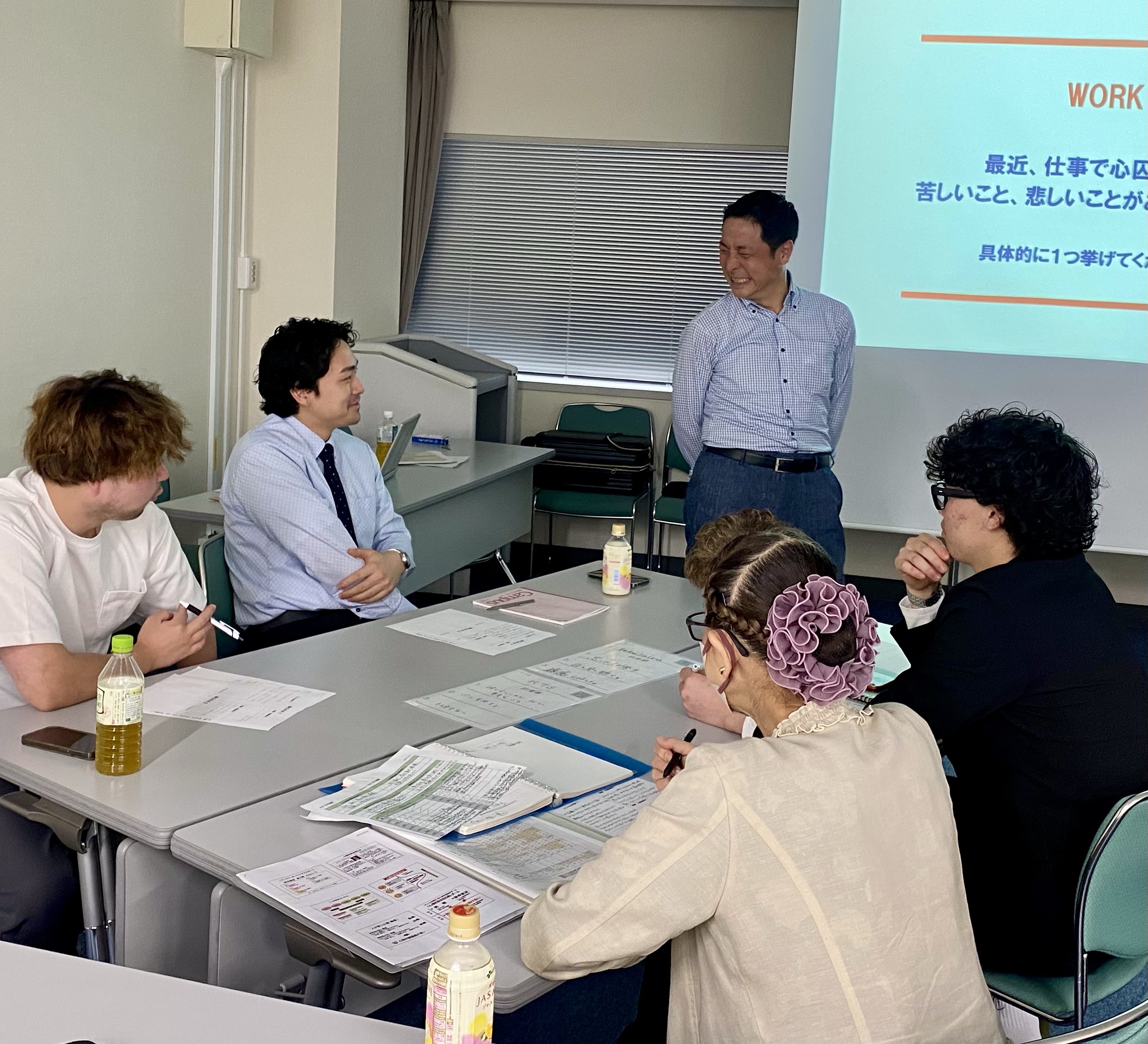 FLM養成講座の様子。講師が笑顔で語りかけ、受講生がグループで耳を傾けている